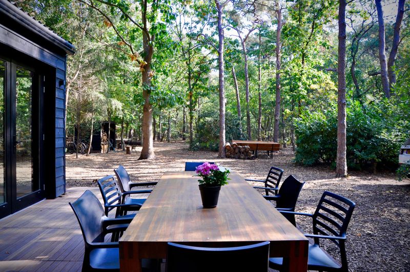 Lange houten buitentafel met acht stoelen op het terras van het boshuisje, omringd door bomen